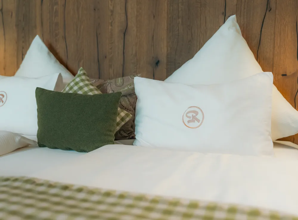 gemutliches-hotelbett-mit-weissen-kissen-grunen-polstern-und-holzruckwand.jpg
